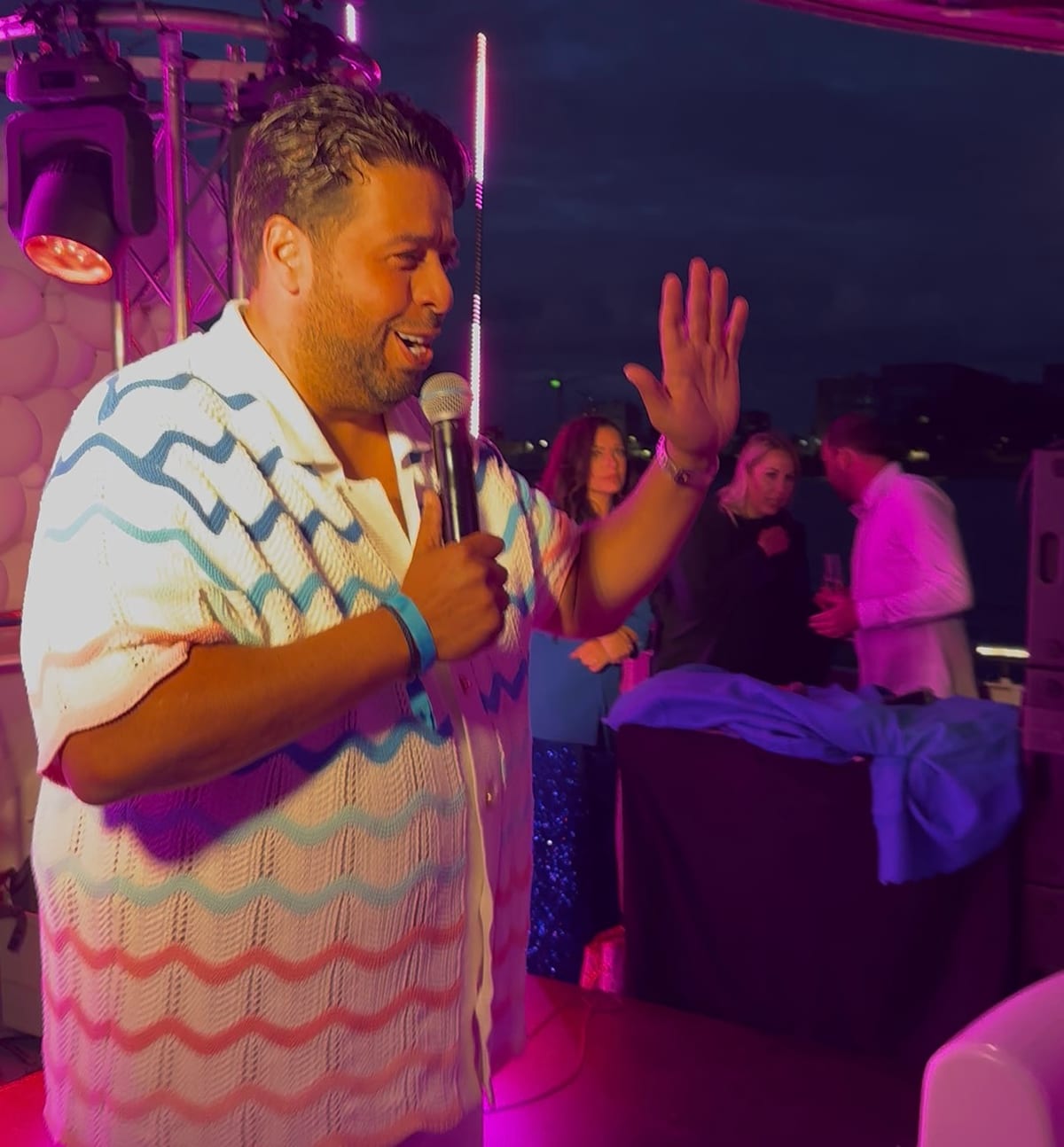 Janah Louard zingt lachend live op een feest, met gasten achter hem